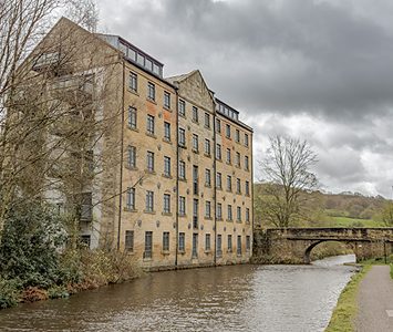 A tall former textile mill standing beside the canal in the Calder Valley, typical of the industrial Calderdale landscape around Halifax