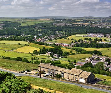 The view from Castle Hill over the Huddersfield valley, with stone farmsteads, green fields and the surrounding Pennine hills beyond
