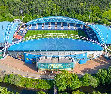 The distinctive arched stands of Huddersfield's stadium, home to the town's football and rugby league teams, beside the River Colne