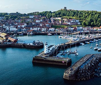 An aerial view of Scarborough harbour and its lighthouse pier, with the old town and castle headland rising behind, near here