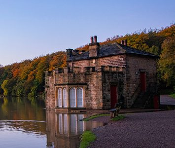 The historic stone boathouse on the water's edge at Newmiller Dam, with autumn woodland rising behind
